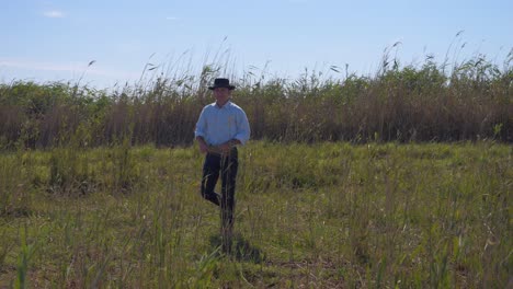 Cowboy-man-walking-in-in-a-field-with-long-grass-in-his-hand
