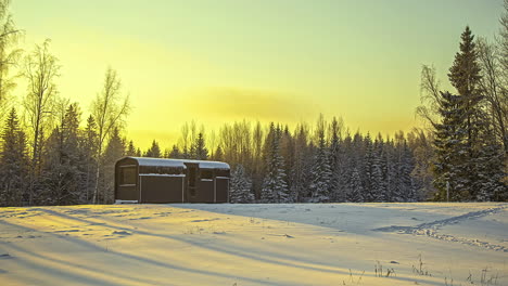 Sunset-over-cabin-in-the-woods-in-snowy-winter-wonderland,-Timelapse