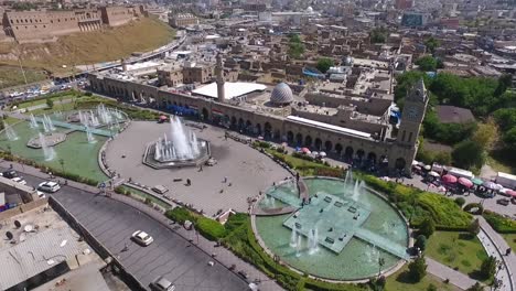 Eine-Luftaufnahme-Der-Stadt-Erbil-Mit-Der-Alten-Zitadelle-Von-Erbil-Und-Dem-Garten-Gegenüber-Dem-Schloss-Mit-Wasserfontänen-Und-Dem-Beliebten-Markt-19