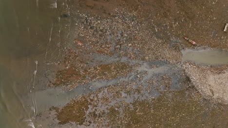 Top-down-aerial-footage-of-a-creek-that-is-depositing-trash-out-into-the-ocean
