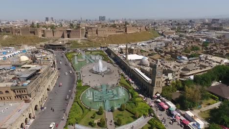 Eine-Luftaufnahme-Der-Stadt-Erbil-Mit-Der-Alten-Zitadelle-Von-Erbil-Und-Dem-Garten-Gegenüber-Dem-Schloss-Mit-Wasserfontänen-Und-Dem-Beliebten-Markt-16