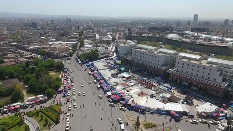 Eine-Luftaufnahme-Der-Stadt-Erbil-Mit-Der-Alten-Zitadelle-Von-Erbil-Und-Dem-Garten-Gegenüber-Dem-Schloss-Mit-Wasserfontänen-Und-Dem-Beliebten-Markt-15