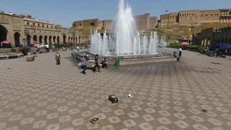 Eine-Luftaufnahme-Der-Stadt-Erbil-Mit-Der-Alten-Zitadelle-Von-Erbil-Und-Dem-Garten-Gegenüber-Dem-Schloss-Mit-Wasserfontänen-Und-Dem-Beliebten-Markt-14