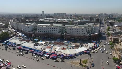 Eine-Luftaufnahme-Der-Stadt-Erbil-Mit-Der-Alten-Zitadelle-Von-Erbil-Und-Dem-Garten-Gegenüber-Dem-Schloss-Mit-Wasserfontänen-Und-Dem-Beliebten-Markt-13