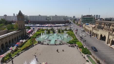 Eine-Luftaufnahme-Der-Stadt-Erbil-Mit-Der-Alten-Zitadelle-Von-Erbil-Und-Dem-Garten-Gegenüber-Dem-Schloss-Mit-Wasserfontänen-Und-Dem-Beliebten-Markt-20