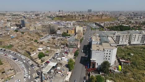 Eine-Luftaufnahme-Der-Stadt-Erbil-Mit-Der-Alten-Zitadelle-Von-Erbil-Und-Dem-Garten-Gegenüber-Dem-Schloss-Mit-Wasserfontänen-Und-Dem-Beliebten-Markt-10