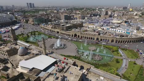 Eine-Luftaufnahme-Der-Stadt-Erbil-Mit-Der-Alten-Zitadelle-Von-Erbil-Und-Dem-Garten-Gegenüber-Dem-Schloss-Mit-Wasserfontänen-Und-Dem-Beliebten-Markt-8