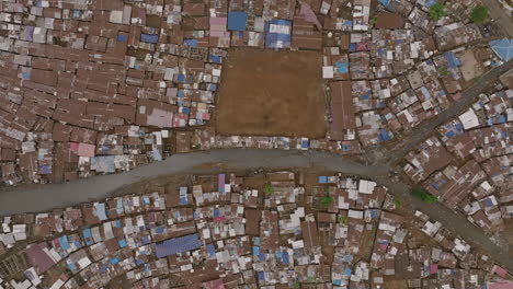 Aerial-top-down-footage-that-descends-towards-a-soccer-field-that-is-next-to-a-creek-surrounded-by-neighborhoods-in-Sierra-Leone