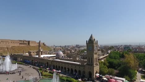 Eine-Luftaufnahme-Der-Stadt-Erbil-Mit-Der-Alten-Zitadelle-Von-Erbil-Und-Dem-Garten-Gegenüber-Dem-Schloss-Mit-Wasserfontänen-Und-Dem-Beliebten-Markt-6