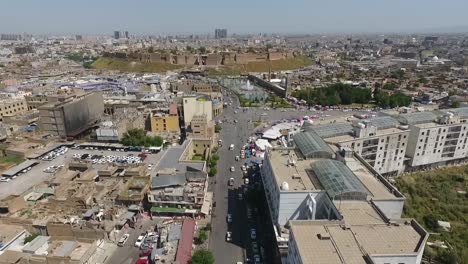 Eine-Luftaufnahme-Der-Stadt-Erbil-Mit-Der-Alten-Zitadelle-Von-Erbil-Und-Dem-Garten-Gegenüber-Dem-Schloss-Mit-Wasserfontänen-Und-Dem-Beliebten-Markt-3