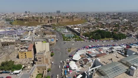 Eine-Luftaufnahme-Der-Stadt-Erbil-Mit-Der-Alten-Zitadelle-Von-Erbil-Und-Dem-Garten-Gegenüber-Dem-Schloss-Mit-Wasserfontänen-Und-Dem-Beliebten-Markt-2