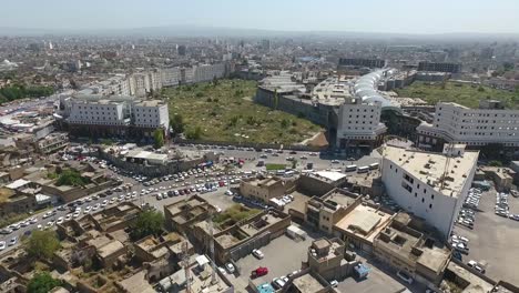 Eine-Luftaufnahme-Der-Stadt-Erbil-Mit-Der-Alten-Zitadelle-Von-Erbil-Und-Dem-Garten-Gegenüber-Dem-Schloss-Mit-Wasserfontänen-Und-Dem-Beliebten-Markt