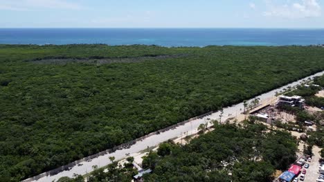 Empty-main-road-in-Tulum-town-leading-to-the-hotel-zone-and-blue-ocean-on-sunny-day,-aerial