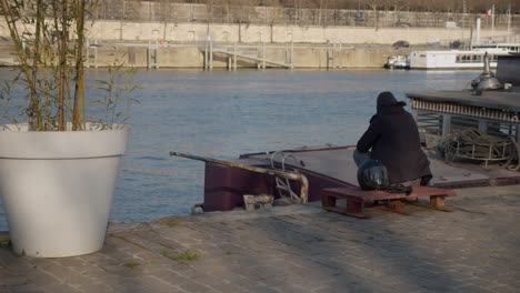 Lonely-person-sitting-on-bench-in-urban-city-pier-of-Paris,-back-view