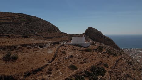 Aerial-view-around-a-chapel-on-a-mountain-in-Santorini,-in-sunny-Greece---circling,-drone-shot