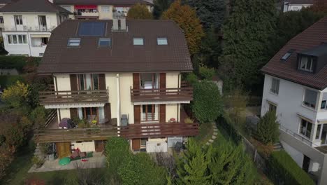 Drone-push-out-aerial-view:-drone-flies-up-and-away-from-a-house,-villa-in-Switzerland-and-reveals-the-surroundings-houses,-garden-and-trees,-Vaud