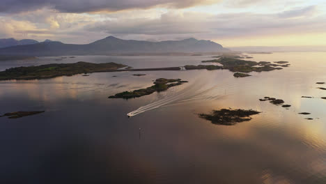 Vista-Aérea-Siguiendo-Un-Barco-Conduciendo-Frente-A-La-Carretera-Del-Océano-Atlántico,-Puesta-De-Sol-En-Noruega