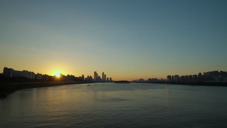 Seoul-sunset---sun-setting-behind-Youido-skyscraper-buildings-and-sunlight-reflection-in-Han-river-water---View-from-Dongjak-bridge