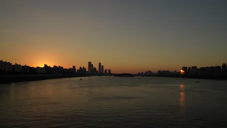 Sunset-Seoul-downtown---sun-hiding-behind-skyscraper-building-and-horizon---view-from-Hanriver-water-front-at-dusk,-South-Korea
