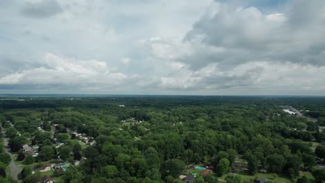 From-a-great-height,-a-drone-captured-the-small-town,-which-is-surrounded-by-tall-trees-and-a-cloudy-sky
