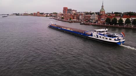 Frachtschiff-Mit-Sand-Durch-Einen-Holländischen-Kanal-Mit-Der-Stadt-Im-Hintergrund