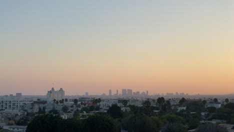 Abendlicher-Blick-Auf-Die-Innenstadt-Von-Los-Angeles-In-Der-Ferne,-Während-Die-Sonne-Mit-Palmen-Untergeht,-Kalifornien,-Usa