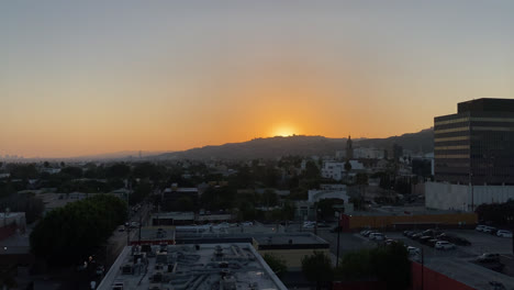 Abendlicher-Blick-Auf-Die-Stadt-Los-Angeles,-Während-Die-Sonne-Hinter-Einem-Hügel-Mit-Bäumen-Untergeht,-Kalifornien,-USA