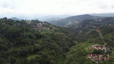 Aerial-shot-of-mountain-valley-with-buildings-and-forest-of-greens