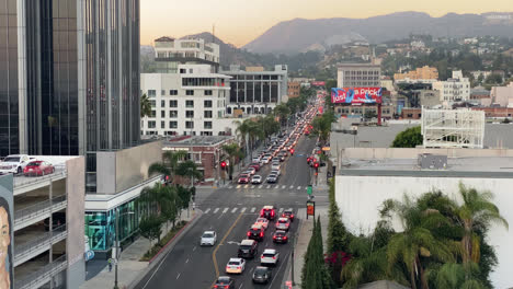 Tráfico-En-La-Intersección-En-El-Centro-De-Los-ángeles-Al-Atardecer-Con-Edificios-Y-Letrero-De-Hollywood-En-Segundo-Plano-En-California,-Estados-Unidos