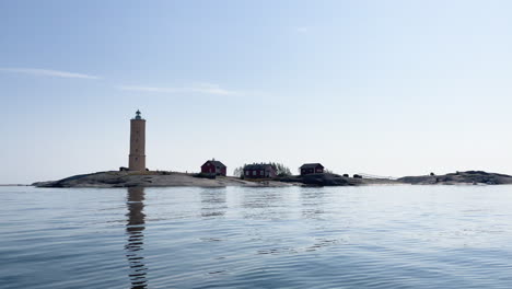 Old-lighthouse-with-small-cottages-on-a-rocky-island-surrounded-by-calm-sea-water