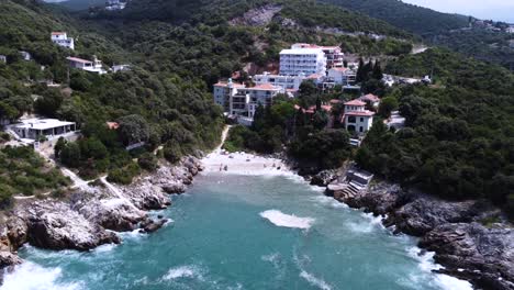 Small-secluded-beach-between-rocks-with-luxury-apartment-buildings,-aerial