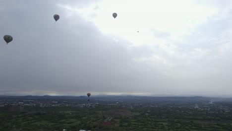 Hot-air-balloons-flying-over-a-gloomy-countryside-of-San-Juan,-Mexico---aerial-view