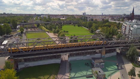 Smooth-aerial-view-flight-subject-out-of-view-drone
of-a-yellow-Train-U-Bahn-on-a-Steel-railroad-bridge-at-Park-on-Gleisdreieck-Berlin-Germany-at-summer-day-2022