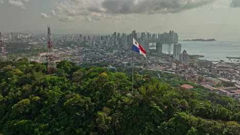 Panama-City-Aerial-V67-Cinematic-Low-Level-Flyover-Ancon-Hill-Mit-Wind,-Der-Die-Nationalflagge-Auf-Einem-Hügel-Weht,-Mit-Stadtbild-Der-Küstenstadt-Im-Hintergrund---Aufgenommen-Mit-Mavic-3-Cine---März-2022