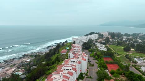 Aerial-view-dolly-in-of-exclusive-buildings-with-tiled-roofs-overlooking-the-sea,-cloudy-day,-Maitencillo,-Chile