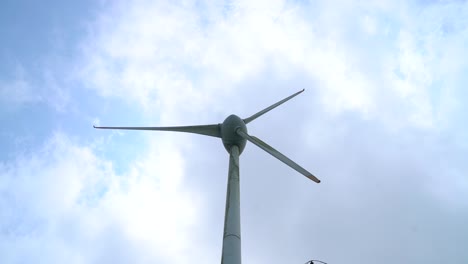 Windturbine-Tower-And-Rotating-Blades-Against-The-White-Clouds-In-The-Sky