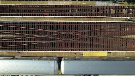 A-top-down-view,-directly-above-elevated-train-tracks-as-a-silver-subway-travels-from-left-to-right-of-the-frame-on-a-sunny-day