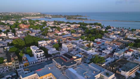 Aerial-flyover-city-of-Santo-Domingo-at-colonial-zone-with-harbor-and-ship-in-background-at-sunset