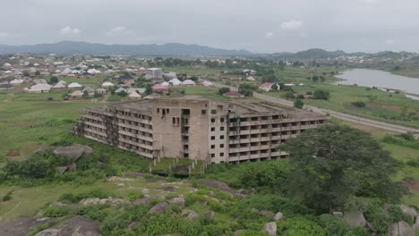 AERIAL---Abandoned-hotel-building-and-Lamingo-Dam,-Jos-Plateau,-Nigeria,-spinning-shot