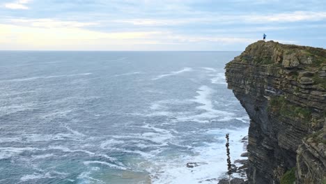 On-a-cloudy-day,-a-man-is-standing-at-the-cliff's-edge-in-Isla,-Cantabria,-and-gazing-out-at-the-endless-blue-sea