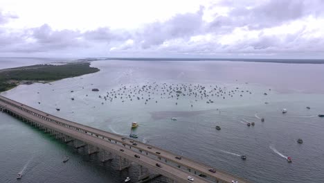 Very-high-drone-view-of-the-Destin-FL-bridge-and-Crab-Island-with-lots-of-cars-and-boats-with-a-cloudy-sky