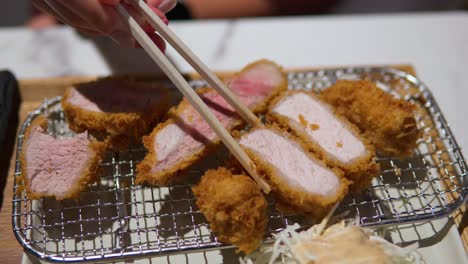 Korean-Woman's-Hand-Picks-up-Tonkatsu-slice,-dips-in-sauce,-and-eats-in-slow-motion---Japanese-Pork-Cutlet