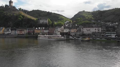 Drone-takes-off-looking-over-the-town-of-Cochem-and-a-riverboat-alongside-on-the-riverbank,