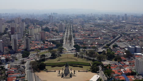 Drone-flying-trough-the-Independence-Monument-in-the-Independence-Park-and-unveiling-the-Avenue-Don-Pedro-I-in-front-of-it-with-the-city-of-SÃ£o-Paulo-on-the-background