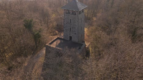 Person-exploring-the-top-level-of-an-old-observation-tower-within-a-dense-but-bare,-brown-forest-in-evening-sunshine