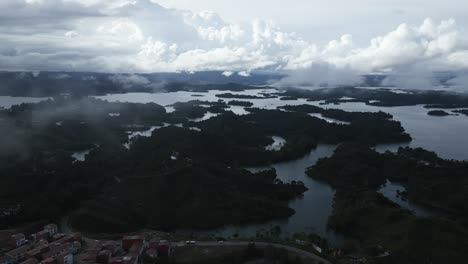 Top-of-El-Penol-Aerial-Drone-Fly-Above-Guatape-Hills-and-Lake-East-Medellin-Sun-Rays-Coming-to-Houses-Through-Misty-Clouds