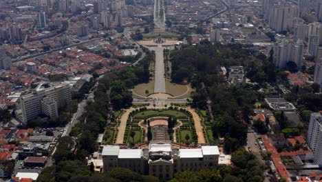 Drone-Volando-A-Través-Del-Museo-Ipiranga-Y-El-Monumento-A-La-Independencia-En-El-Parque-De-La-Independencia-Y-Revelando-La-Avenida-Don-Pedro-I-Frente-A-Ella-Con-La-Ciudad-De-São-Paulo-Al-Fondo