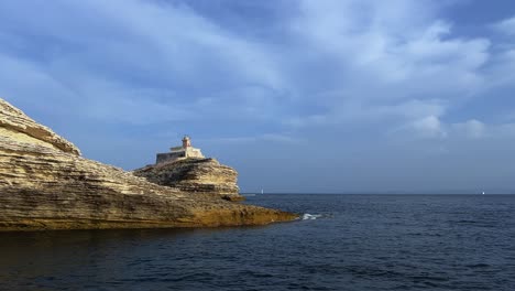 Madonnetta-lighthouse-perched-on-cliff-along-Southern-Corsica-island-coastline-in-France-seen-from-sailing-boat