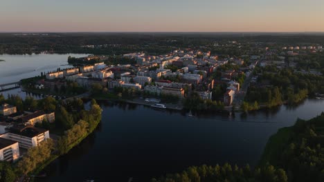 Aerial-view-of-a-boat-passing-the-cityscape,-driving-in-tranquil-waters-of-lake-Vanajavesi,-summer-sunset-in-Hameenlinna,-Finland