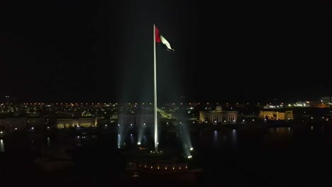 4K:-Aerial-night-view-of-the-Flag-of-the-United-Arab-Emirates-waving-in-the-air,-The-national-symbol-of-the-United-Arab-Emirates